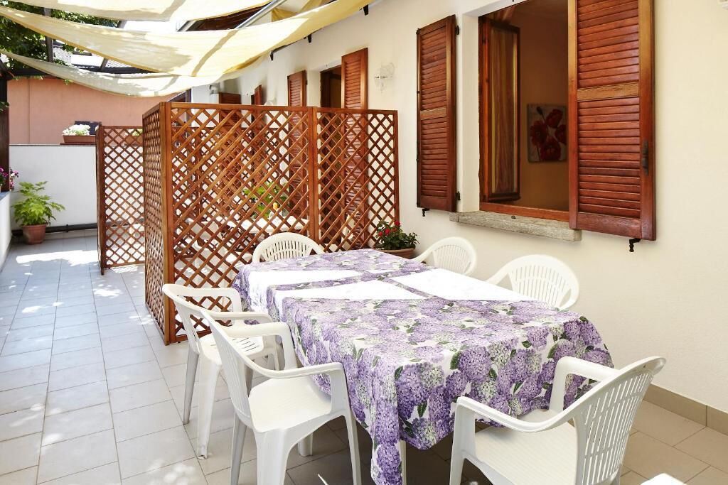 Un patio exterior con una mesa lista para cuatro personas, rodeado de sillas blancas y un panel de madera celosía.