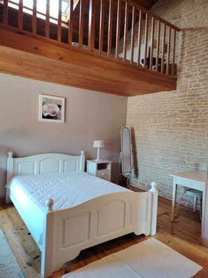 A bedroom with a wooden ceiling, a white bed, a bedside table with a lamp, a small desk with a chair, and a stone wall. - Longère in the heart of the marsh with private port (Arçais)