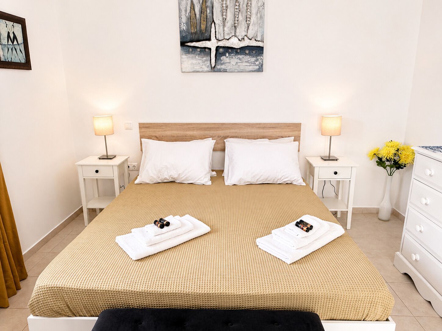 Habitación de hotel con una cama grande, dos mesitas de noche, un cabecero de madera, ropa de cama blanca y un cuadro en la pared.