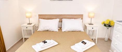 A hotel room with a large bed, two bedside tables, a wooden headboard, white bedding, and a painting on the wall.