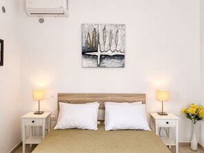 Ein Schlafzimmer mit einem Bett, zwei Nachttischen, zwei Lampen, einer Wandklimaanlage und einem Gemälde.