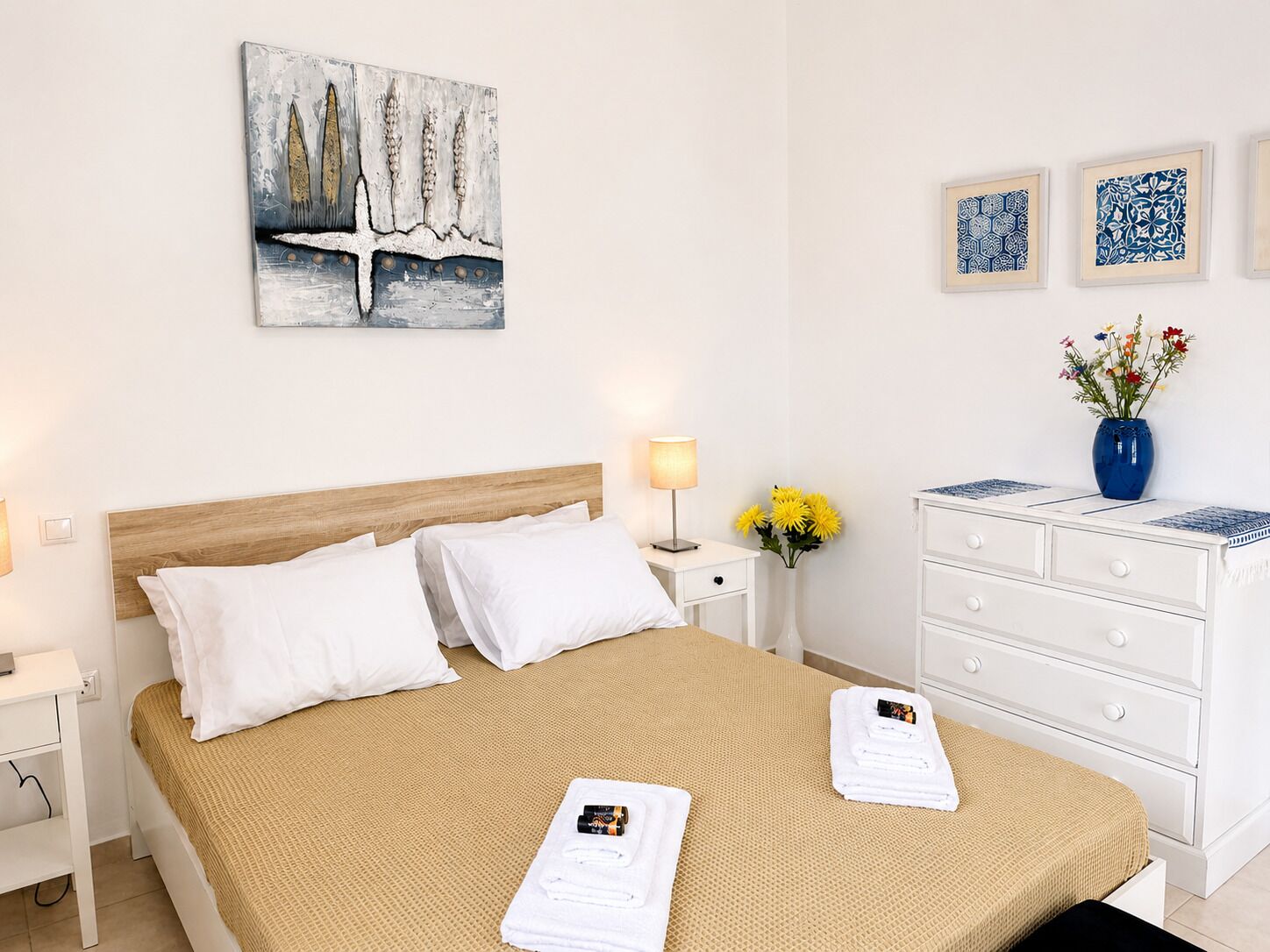 Une chambre d’hôtel comprenant un lit, une table de chevet, une lampe, une commode et un mur décoré d’œuvres d’art.