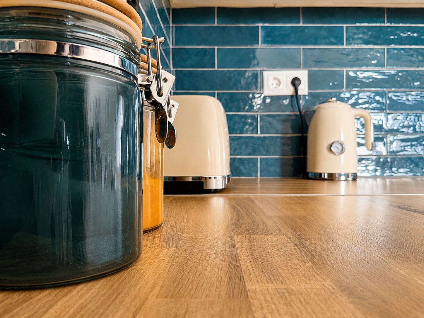 A kitchen with a large glass jar, a toaster, and a kettle on a wooden countertop.
