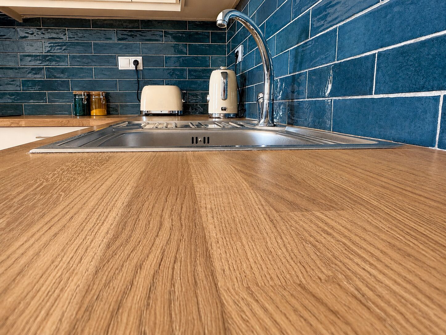 A kitchen with a wooden countertop, a stainless steel sink, a toaster, and a blue tiled backsplash.
