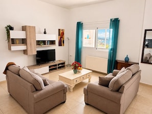 A living room with a TV, two sofas, a coffee table, and a window with curtains. - Sea to Summit Terrace 2BD 1BA 7mn to Georgioupoli (Apokoronas)