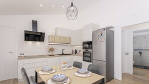 A modern kitchen with white cabinetry, a stainless steel refrigerator, and a dining area with a wooden table set for four. - Villa Aurora with private pool (Tertenia)