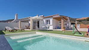 A poolside area with a clear pool, lounge chairs, a pergola, and a small slide. - Villa Aurora with private pool (Tertenia)