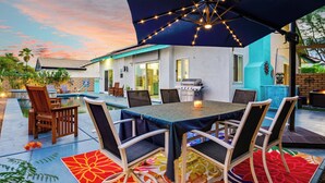 An outdoor patio with a pool, dining table, chairs, and string lights. - Casa Solara - A Ryson Property (Palm Springs)