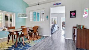 A modern living room with a dining area, a hallway leading to another room, and a sign indicating a location. - Casa Solara - A Ryson Property (Palm Springs)