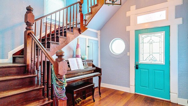 A grand staircase leading to a piano in a room with a teal door and a decorative window.