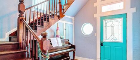 Una gran escalera con un piano, una puerta color turquesa y una araña.