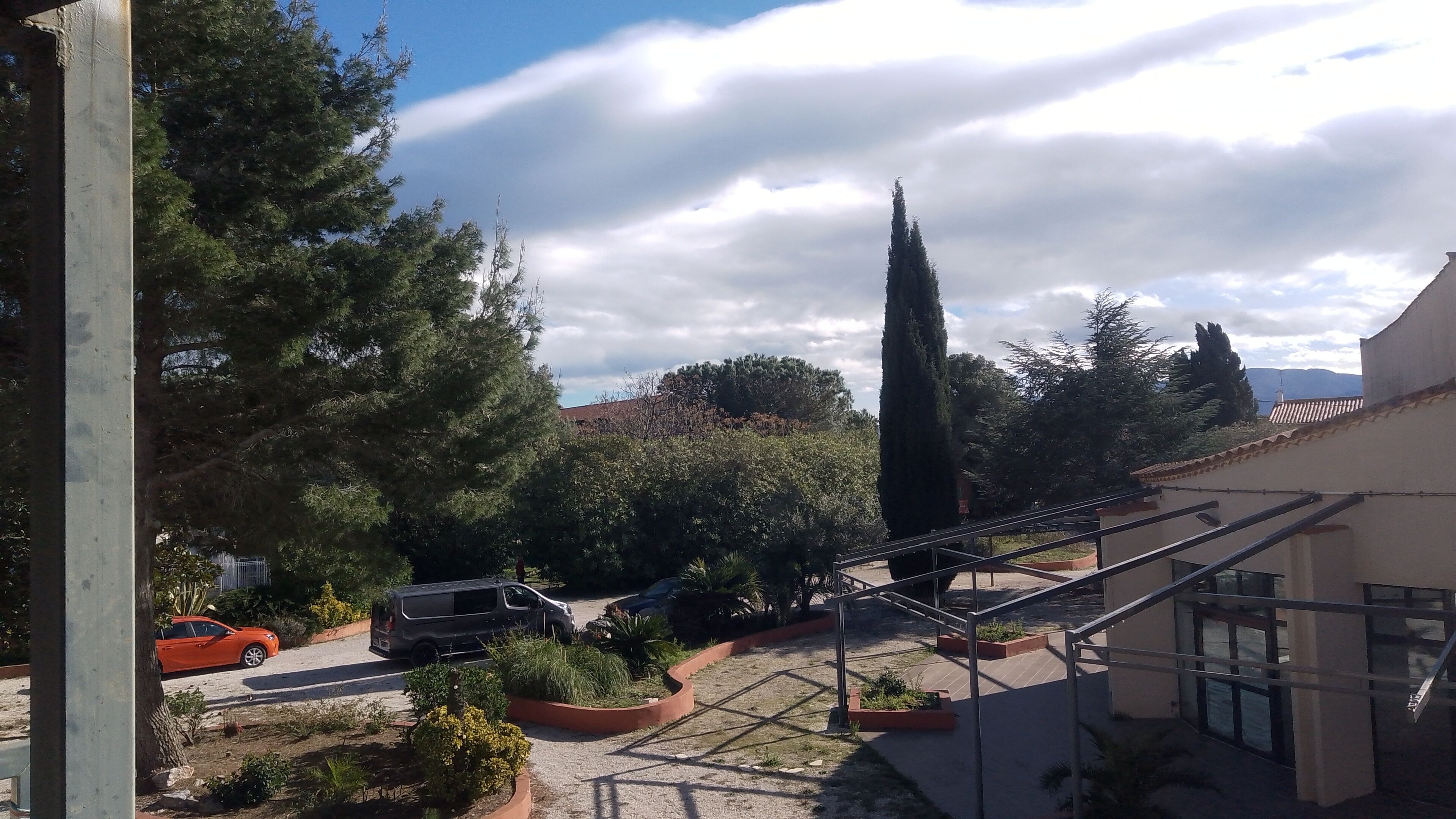 Une cour intérieure avec une voiture garée près d’un bâtiment, le tout entouré d’arbres et de plantes.