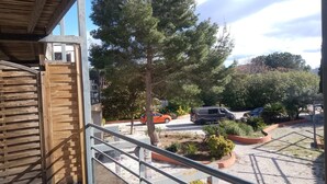 A balcony with a wooden railing overlooking a parking area with several cars and greenery.