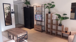 Una sala de estar moderna con una mesa de centro de madera, un mueble negro, un televisor sobre un soporte de madera y una estantería con plantas.