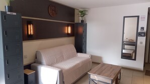 A hotel room with a sofa, a small table, a mirror, and a set of lockers.