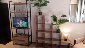 A living room with a TV on a wooden shelf, a potted plant, and a lamp on a side table.