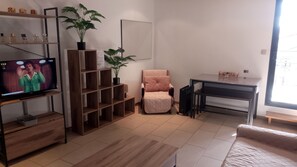 Una sala de estar con televisión, estanterías de madera, una silla, una mesa y plantas en macetas.