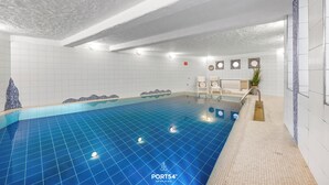 An indoor swimming pool with a blue tiled floor, white walls, and a seating area with chairs and a small plant. - Linda - Balcony with sea view, private beach chair on the beach, swimming pool (Kronsgaard)