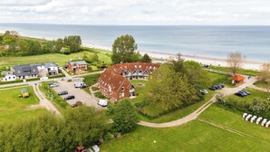 An aerial view of a coastal property with multiple buildings, a parking area, and a beach in the background. - Linda - Balcony with sea view, private beach chair on the beach, swimming pool (Kronsgaard)