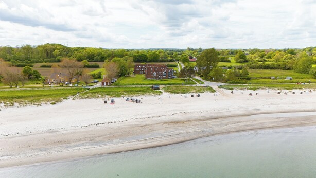 A coastal hotel with a beach view, a parking area, and a large building with multiple windows. - Linda - Balcony with sea view, private beach chair on the beach, swimming pool (Kronsgaard)