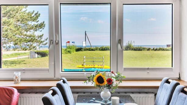 Ein Zimmer mit Tisch und Stühlen, einer Blumenvase und Blick auf Strand und Flagge.