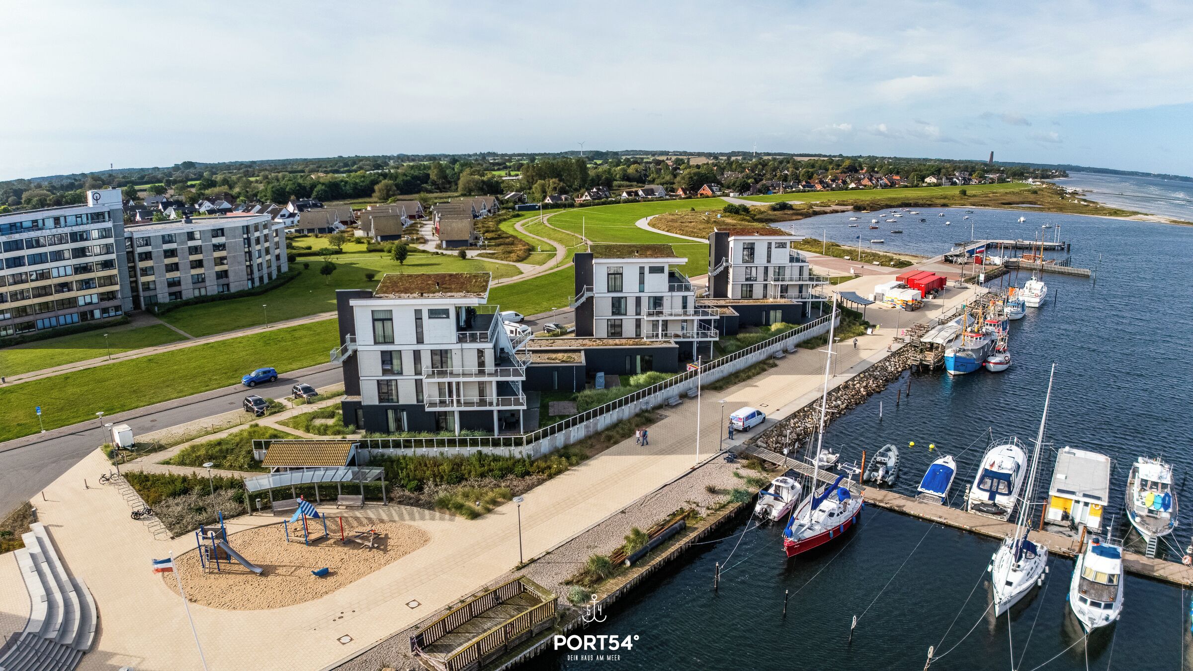 Un port de plaisance moderne, avec des bateaux amarrés, une aire de jeux et des immeubles résidentiels.
