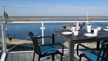 A deck with a table set for dining, overlooking a calm body of water and a distant shoreline.