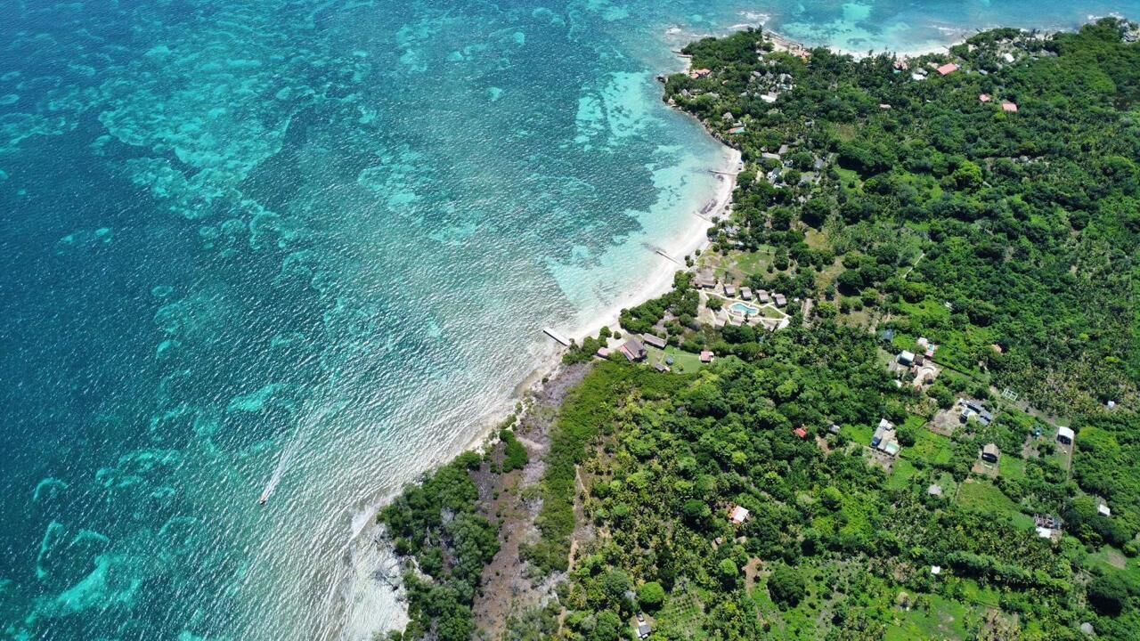 Vue aérienne d’une zone côtière avec une plage et quelques bâtiments dispersés.