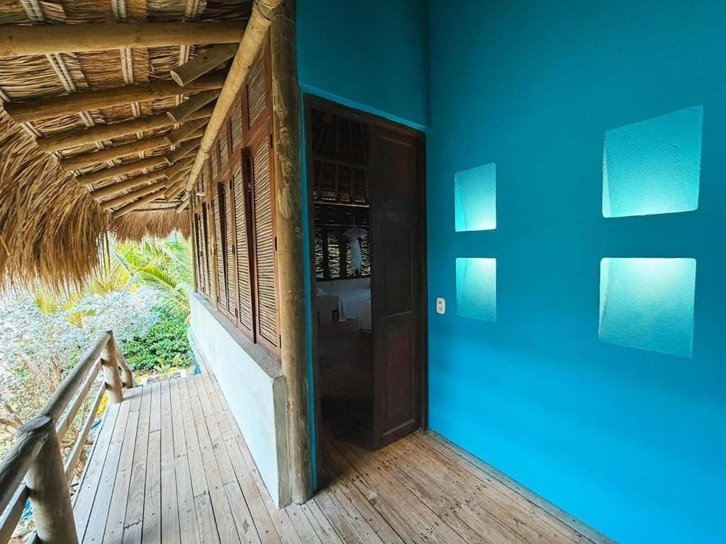 A wooden deck with a thatched roof, a blue wall with square cutouts, and a door leading to a room with a visible closet.