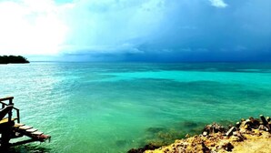 Une jetée en bois s’étendant dans une mer turquoise, avec une côte rocheuse au premier plan.