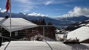 A snow-covered mountain landscape with a clear sky and a flag on a pole. - swissmountainview - sunny & quiet - terrace, Jacuzzi, view to lake + mountains (Beatenberg)