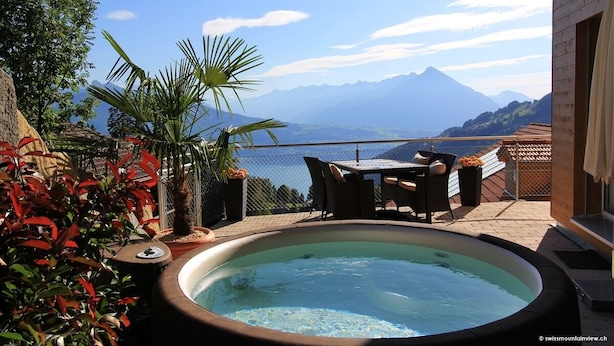 A hot tub with a mountain view, surrounded by plants and outdoor furniture. - swissmountainview - sunny & quiet - terrace, Jacuzzi, view to lake + mountains (Beatenberg)
