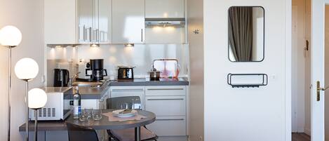 A compact kitchen with modern appliances, a dining area with a round table, and a living space with a sofa.