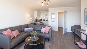 A modern living room with a grey sofa, a round coffee table, and a kitchen in the background. - Welcome to the Best View apartment (List auf Sylt)