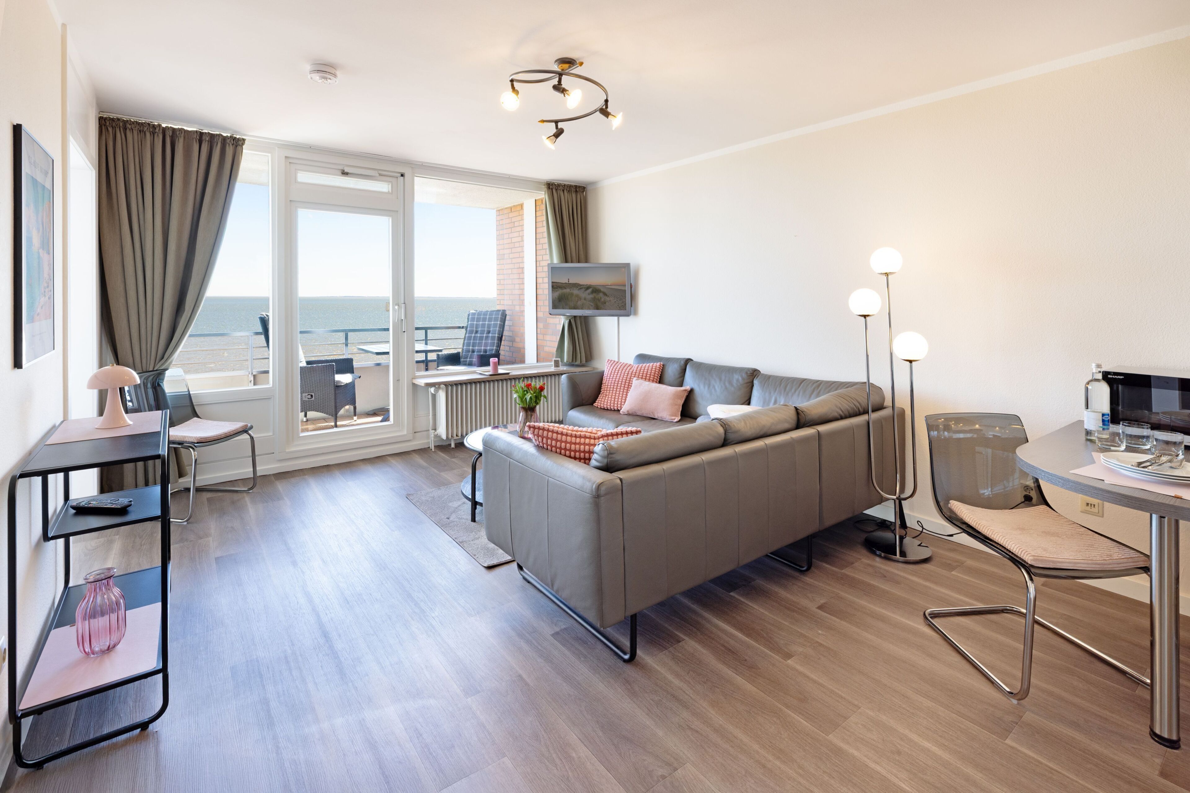 A modern living room with a sofa, a dining table, a TV, and a view of the sea.
