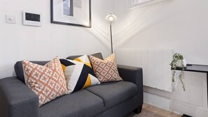 A modern living room with a grey sofa, patterned cushions, a floor lamp, a radiator, and a framed artwork on the wall. - Comfortable 1 Bed Studio, 10/10 Location (Nottingham)