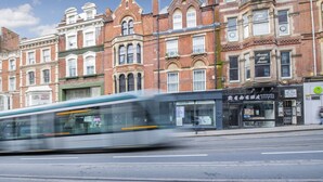 A tram moving past a row of historic brick buildings with large windows and shop fronts. - Comfortable 1 Bed Studio, 10/10 Location (Nottingham)