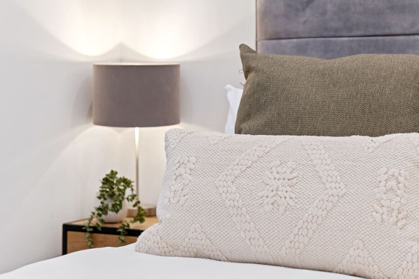 A neatly made bed with a white pillow and a grey pillow.