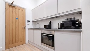 Uma cozinha compacta com armários brancos, forno de aço inoxidável, micro-ondas e cafeteira na bancada.