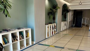 Un pasillo amplio con piso de baldosas, estanterías blancas con libros y plantas en macetas.