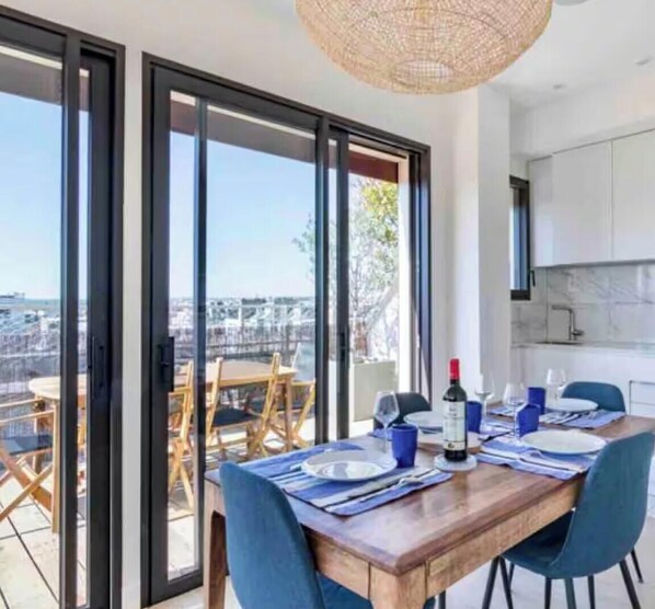 A dining area with a wooden table set for four, a bottle of wine, and a view of the city through large glass doors. - Apartment with large terrace facing the Eiffel Tower. One of a kind! (Neuilly-sur-Seine)