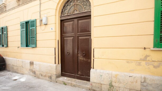 Ein Gebäude mit einer großen, dunkelbraunen Tür, grünen Fensterläden und einem kleinen Fenster mit einem Metallgitter.