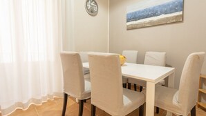 Ein Essbereich mit einem weißen Tisch und Stühlen, einer Uhr an der Wand und einem Bild mit einer Strandansicht.