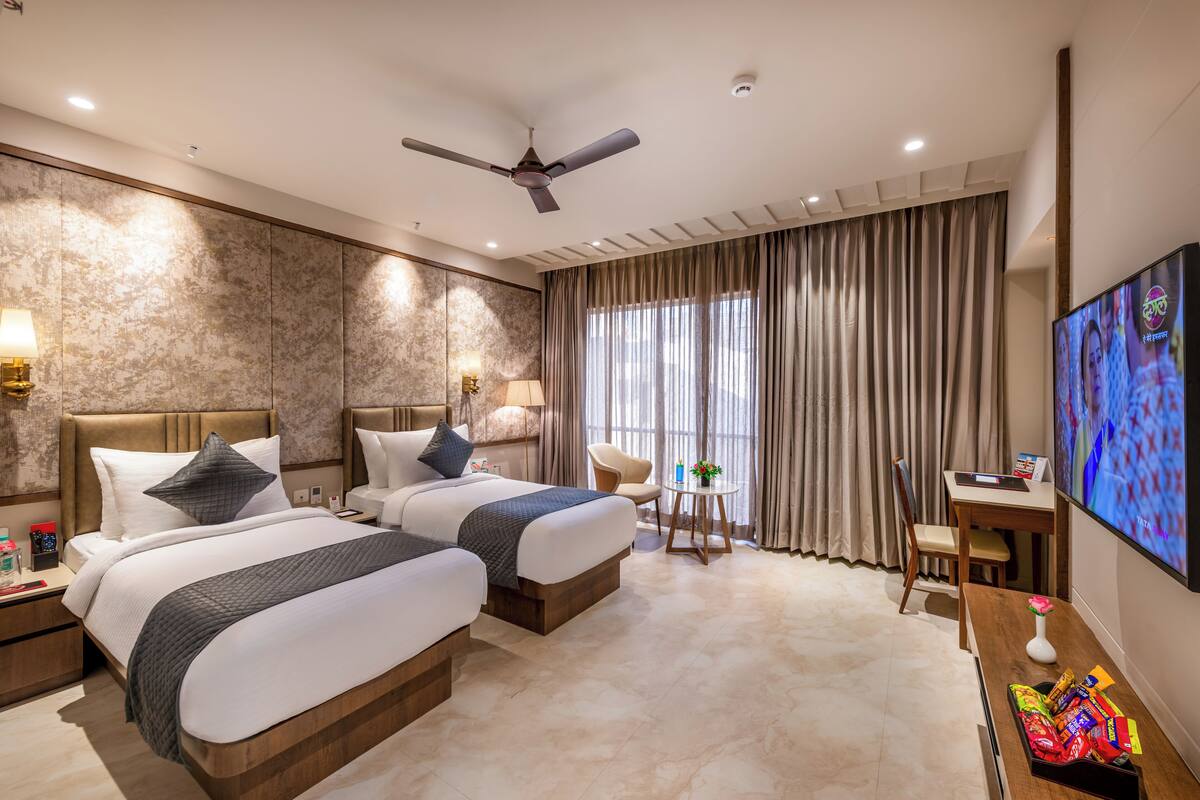 A hotel room with two beds, a desk, a chair, a TV, and a ceiling fan.