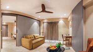 Uma sala de estar moderna com um sofá, uma mesa de jantar, um ventilador de teto e uma fruteira sobre uma mesa de centro.