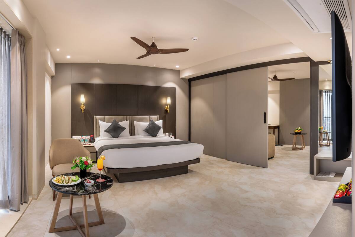 A modern hotel room with a large bed, a sitting area with a table, and a ceiling fan.