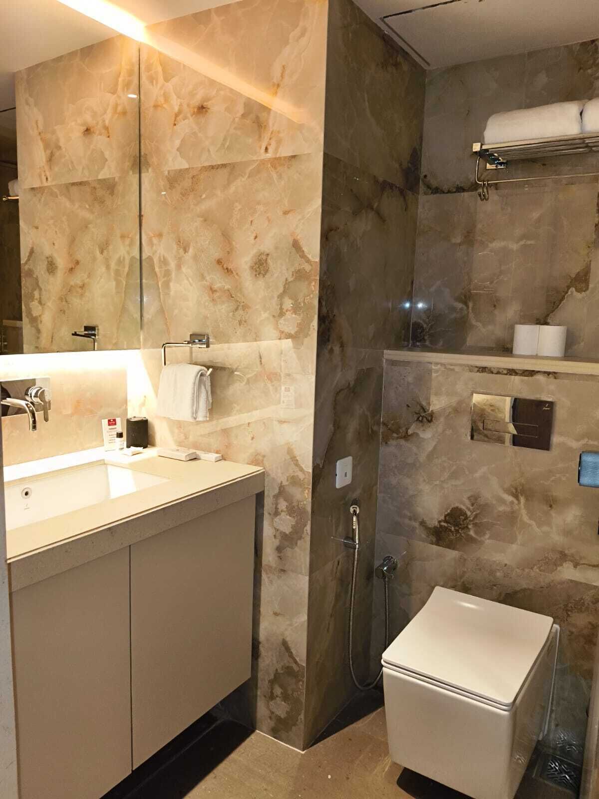 A modern bathroom with a marble wall, a sink, a toilet, and a shower.