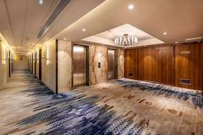 A hotel hallway with elevators, a patterned carpet, and a chandelier. - SkkyLight Lords Inn (Nanded)