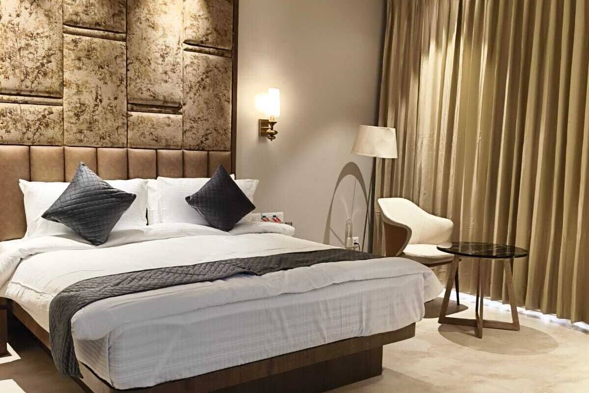A modern hotel room with a large bed, a ceiling fan, a bedside table, and a chair.
