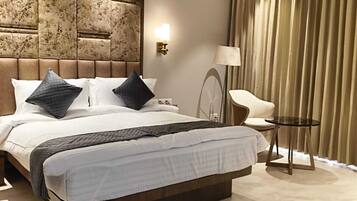 A modern hotel room with a large bed, a ceiling fan, a bedside table, and a chair.